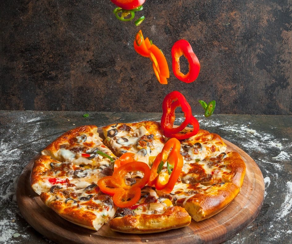 Side view pizza with slices of bell pepper and pizza slices and flour in board cookware on stone background